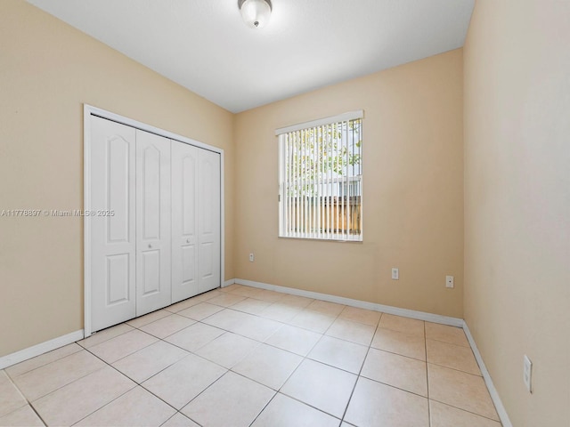 unfurnished bedroom with a closet, light tile patterned flooring, and baseboards