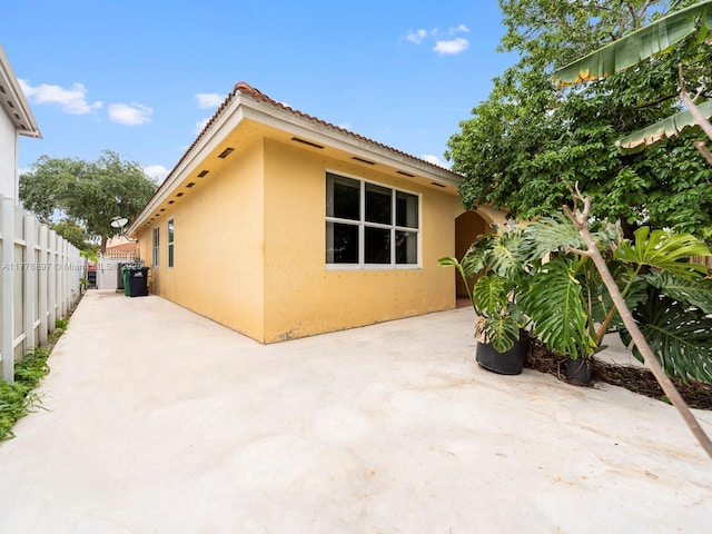 view of side of property with a patio area, stucco siding, a tiled roof, and fence