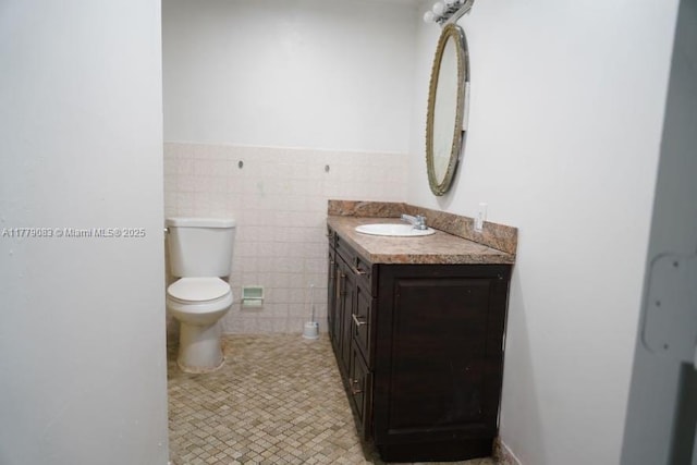 bathroom featuring toilet, tile walls, a wainscoted wall, vanity, and tile patterned floors