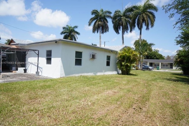back of house with a wall mounted air conditioner, stucco siding, and a lawn