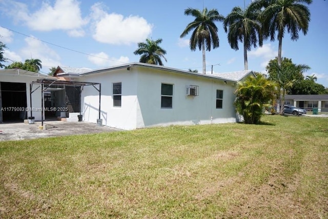 rear view of property with a wall mounted AC, a yard, and stucco siding
