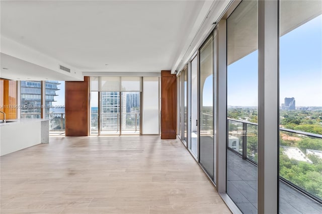 spare room with floor to ceiling windows, a wealth of natural light, light wood finished floors, and visible vents