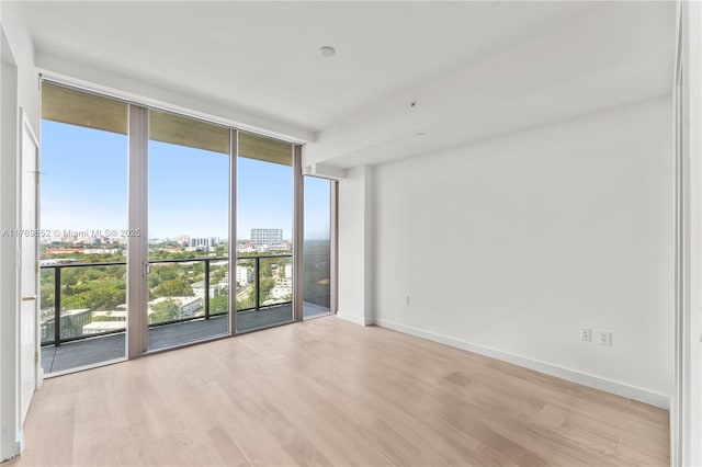 empty room with light wood-style floors, a city view, expansive windows, and baseboards