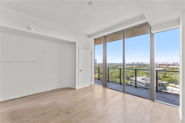 empty room featuring a city view, light wood-type flooring, and a wall of windows