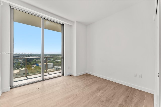 empty room featuring baseboards, wood finished floors, and a wall of windows