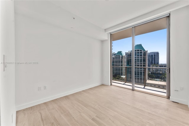 empty room with a wall of windows, a view of city, wood finished floors, and baseboards