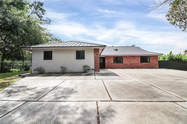 back of property featuring metal roof, fence, stucco siding, brick siding, and a standing seam roof
