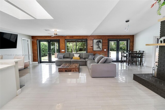 living room featuring french doors, wooden walls, visible vents, and lofted ceiling with skylight