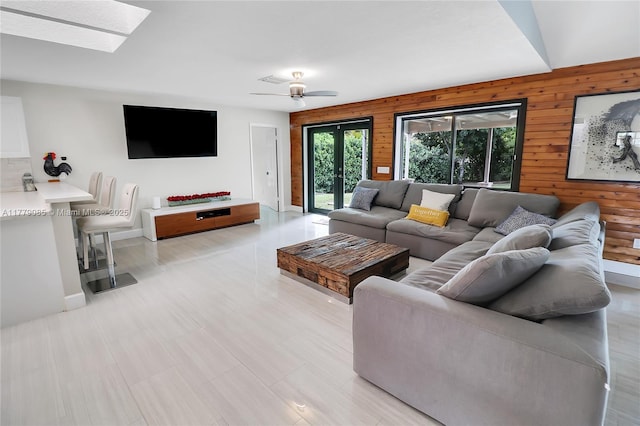 living room featuring wood walls, french doors, a ceiling fan, and a skylight