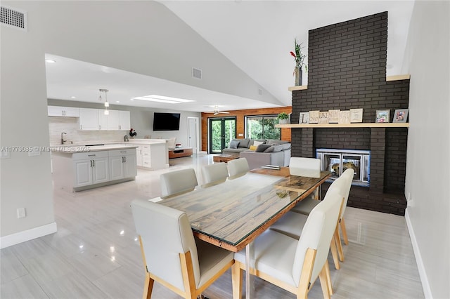 dining area featuring baseboards, high vaulted ceiling, a brick fireplace, and visible vents