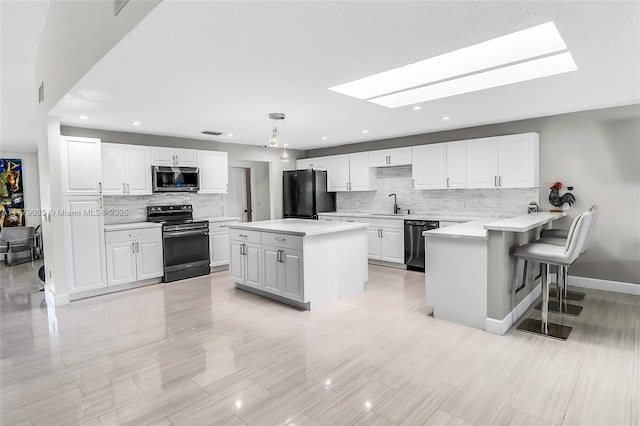 kitchen with a sink, appliances with stainless steel finishes, a peninsula, white cabinetry, and a skylight