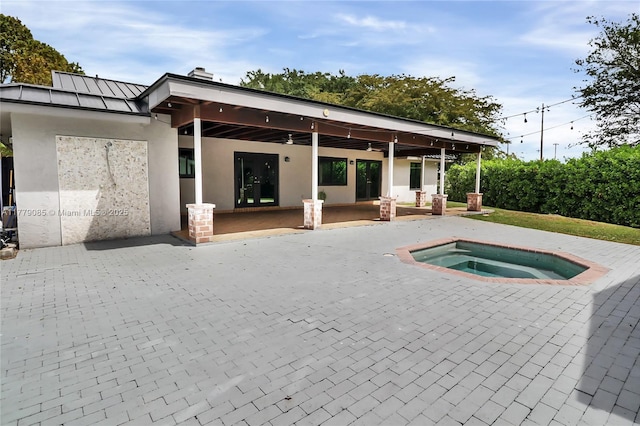 back of house featuring a patio area, an in ground hot tub, a standing seam roof, and stucco siding