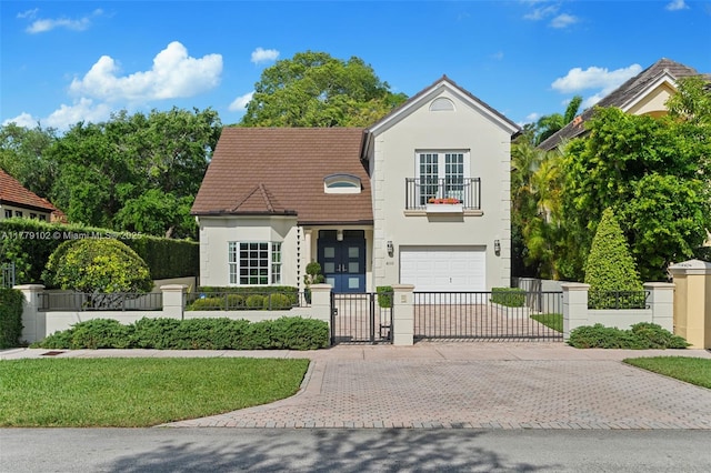traditional-style home with an attached garage, a balcony, a fenced front yard, a gate, and decorative driveway