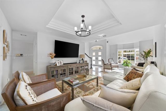 living room featuring a tray ceiling, an inviting chandelier, and visible vents