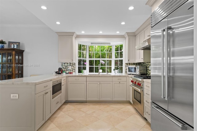 kitchen with a peninsula, ornamental molding, under cabinet range hood, built in appliances, and backsplash