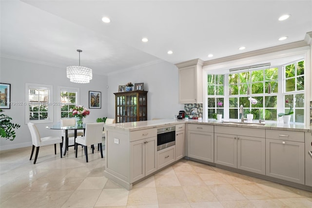 kitchen with a notable chandelier, ornamental molding, a peninsula, stainless steel oven, and a sink