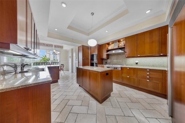 kitchen featuring brown cabinetry, a sink, a raised ceiling, and stainless steel cooktop