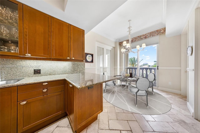 kitchen featuring light stone countertops, a notable chandelier, brown cabinetry, and glass insert cabinets