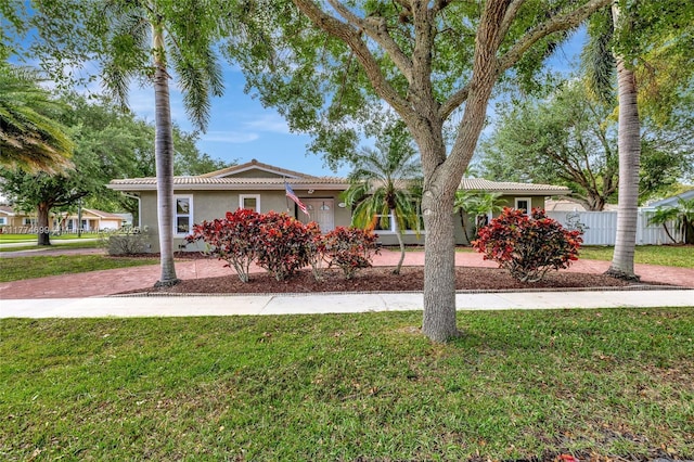 ranch-style house featuring a tile roof, stucco siding, fence, and a front lawn