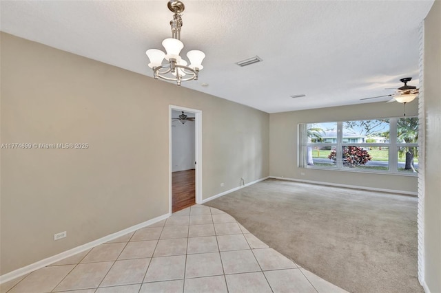 empty room with baseboards, light carpet, light tile patterned flooring, visible vents, and ceiling fan with notable chandelier