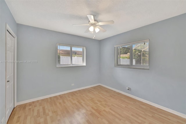 spare room with light wood-style floors, baseboards, a ceiling fan, and a textured ceiling