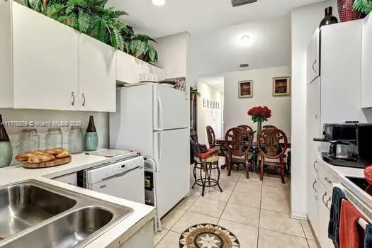 kitchen with white appliances, light countertops, white cabinetry, and light tile patterned flooring