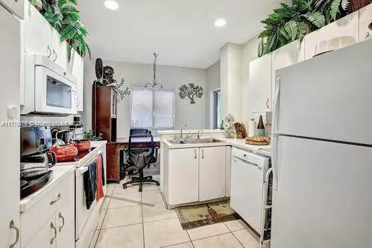kitchen featuring light tile patterned floors, a sink, light countertops, white appliances, and white cabinetry