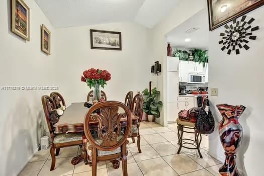 dining area with visible vents, light tile patterned floors, and vaulted ceiling