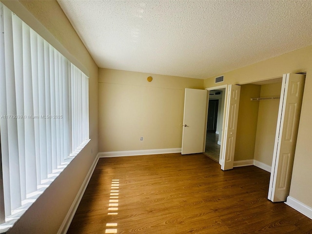 unfurnished bedroom with a textured ceiling, baseboards, dark wood finished floors, and visible vents
