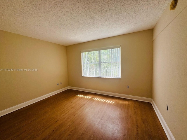 empty room featuring dark wood-type flooring, a textured ceiling, and baseboards