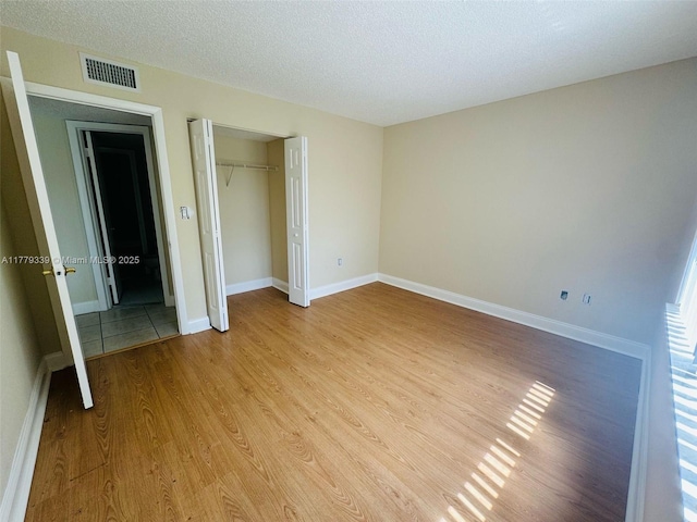 unfurnished bedroom featuring a closet, baseboards, a textured ceiling, visible vents, and light wood finished floors