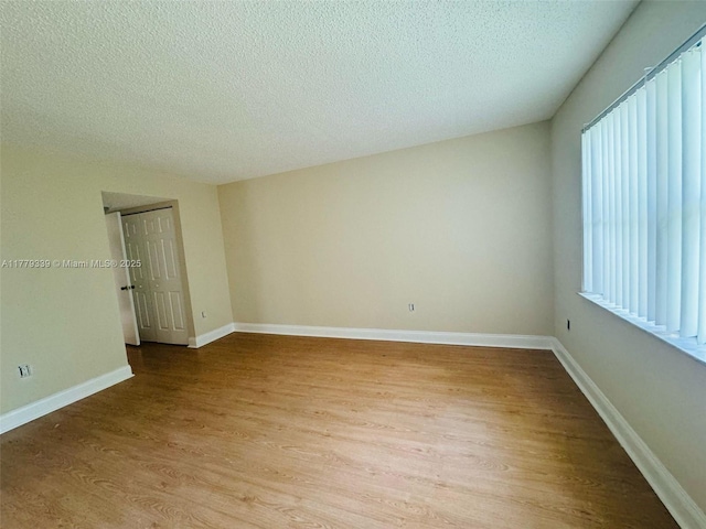 spare room with baseboards, light wood finished floors, and a textured ceiling
