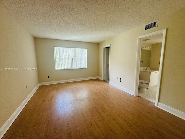 unfurnished room with visible vents, wood finished floors, and a textured ceiling