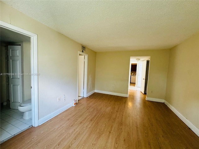 empty room featuring a textured ceiling, wood finished floors, and baseboards