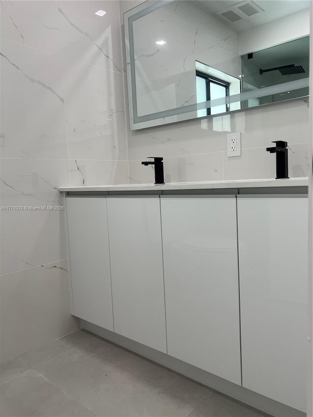 bathroom with double vanity, a sink, visible vents, and tile walls