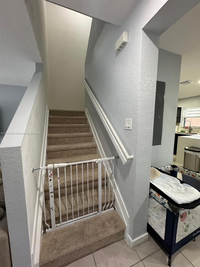 stairs featuring tile patterned floors, a textured wall, baseboards, and electric panel