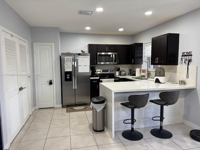 kitchen featuring dark cabinets, a peninsula, visible vents, a sink, and stainless steel appliances