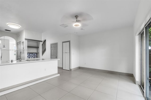unfurnished living room with ceiling fan, arched walkways, visible vents, a sink, and baseboards