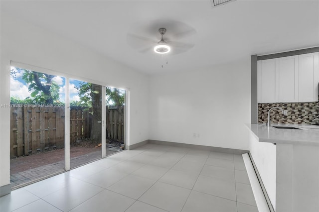 unfurnished dining area with light tile patterned flooring, ceiling fan, a sink, and baseboards