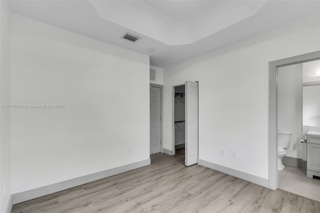 unfurnished bedroom with visible vents, light wood finished floors, a closet, and ensuite bath