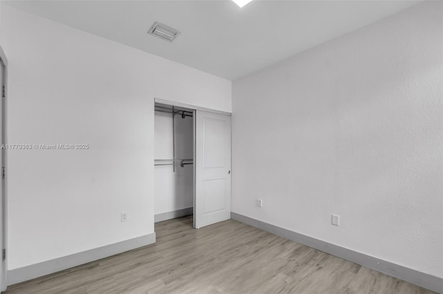 unfurnished bedroom with a closet, visible vents, baseboards, and wood finished floors