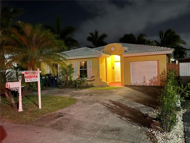 ranch-style home featuring stucco siding, an attached garage, a tiled roof, and aphalt driveway