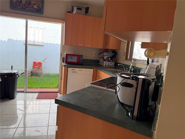 kitchen with dark countertops, dishwasher, light tile patterned floors, and a sink