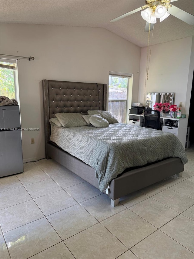 bedroom featuring vaulted ceiling, freestanding refrigerator, tile patterned flooring, and a ceiling fan