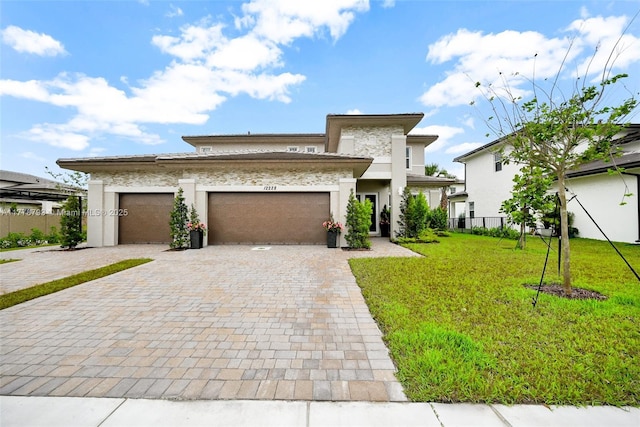 prairie-style home featuring stucco siding, decorative driveway, fence, a front lawn, and a garage