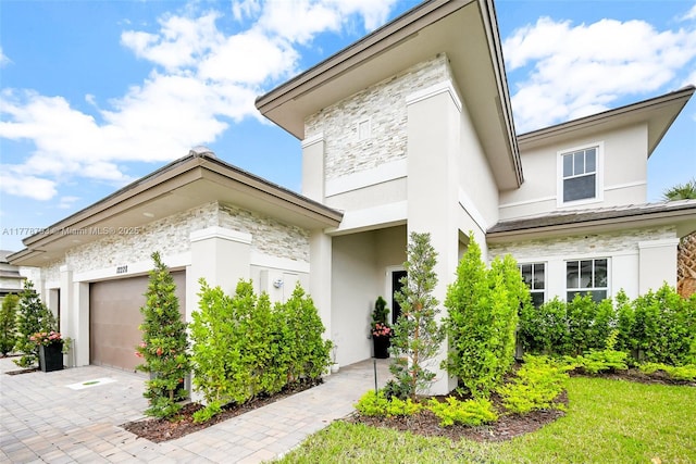 view of front facade featuring an attached garage, driveway, stucco siding, and stone siding
