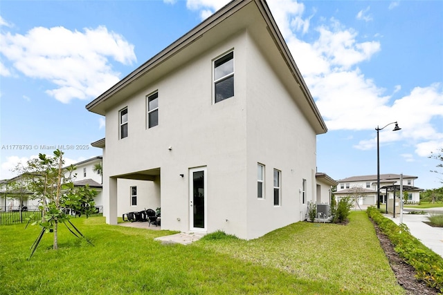 rear view of property featuring a patio, stucco siding, central AC, and a lawn