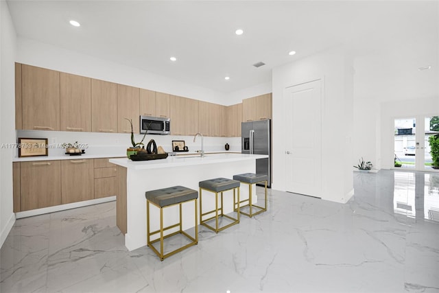 kitchen featuring recessed lighting, modern cabinets, a kitchen bar, appliances with stainless steel finishes, and marble finish floor