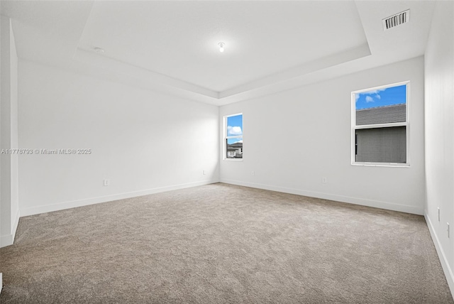 carpeted spare room featuring visible vents, a tray ceiling, and baseboards