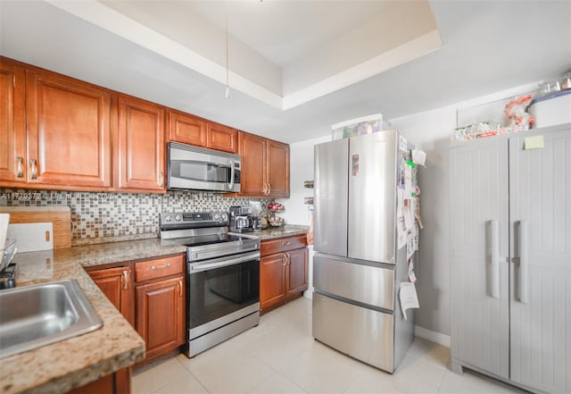 kitchen with decorative backsplash, brown cabinets, light tile patterned floors, a raised ceiling, and stainless steel appliances